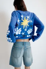Remera oversize de manga larga color azul, con efecto lavado, cuello redondo y detalle de estampación inspirada en Henri Matisse con una estrella amarilla en el pecho y formas abstractas blancas en la manga.