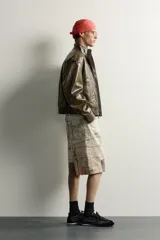 Cazadora cropped fit de color verde militar, confeccionada en tejido efecto piel. Presenta cuello subido, manga larga con puño abotonado, trabillas en los hombros, y bolsillos delanteros de plastrón con solapa. Su diseño incluye bajo elástico y cierre frontal con cremallera oculta por solapa con botones a presión.