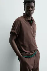 Polo de hombre de corte relajado, color marrón oscuro, confeccionado en tejido texturizado con rayas verticales. Posee cuello solapa y cierre frontal con botonadura oculta por solapa.