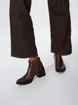 Botinetas de cuero color marrón con diseño bicolor, combinando cuero liso en el cuerpo y textura tipo reptil en la puntera y el talón. Presentan taco cuadrado negro, suela de goma y cierre lateral.