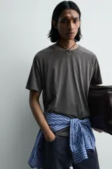 Camiseta relaxed fit color gris oscuro, confeccionada en tejido ligero de algodón con elasticidad. Presenta cuello redondo y manga ranglán corta.