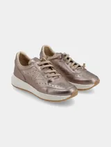 Sneaker de mujer con acabado metalizado en tono dorado, diseño con perforaciones decorativas en los laterales y cordones al tono. Presenta una suela de plataforma blanca con efecto moteado y base de goma color caramelo.