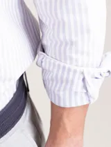 Camisa de hombre Oxford a rayas celestes y blancas, confeccionada en 93% algodón y 7% algodón reciclado. Corte regular fit, cuello button-down, cierre con botones, manga larga con puño simple y logo bordado en el pecho.