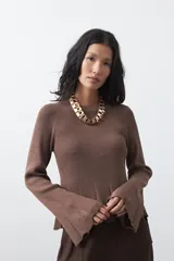 Top de tejido acanalado con sutil acabado metalizado, de silueta entallada con diseño peplum en la cintura y mangas largas levemente acampanadas.