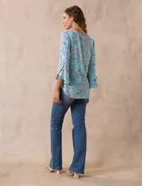 Blusa de seda fría estampada con flores en tonos celeste, lila y verde. Tiene cuello redondo con escote en V entrelazado y mangas 3/4 acampanadas.