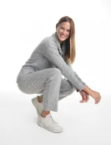 Buzo de tejido suave color gris melange, con cuello volcado ajustable mediante cordones con punteras metálicas. Presenta mangas largas con puños anchos decorados con botones metálicos, hombros caídos y silueta holgada con ruedo redondeado y aberturas laterales.