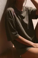 Remera oversize de color marrón grisáceo con efecto lavado, cuello redondo y manga corta. Cuenta con múltiples aplicaciones de brillos con motivos de Hello Kitty, estrellas, cerezas y moños.