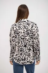 Camisa de manga larga con cuello clásico y cierre frontal de botones. Presenta un estampado de manchas tipo animal print en tonos blanco y negro.