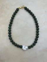 Collar artesanal compuesto por cuentas de piedra volcánica en diversos tonos y tamaños, con una perla natural de río como dije central y cierre metálico dorado.