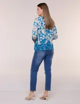 Blusa de silueta holgada y corte recto con caída fluida, escote redondo y mangas largas con puños anchos estructurados, con estampado floral en tonos pasteles sobre fondo blanco.
