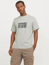 Remera color verde claro de manga corta y cuello redondo con estampado en el pecho con el logo de la marca Jack & Jones y un diseño abstracto en tonos grises y negros.