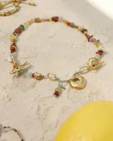 Collar corto de estilo artesanal, compuesto por una variedad de piedras naturales en tonos tierra, verdes, rojos y amarillos, intercaladas con pequeñas perlas de río. Presenta dijes de bronce macizo con formas orgánicas, incluyendo una figura de pez y un dije circular central, unidos por un cierre de barra y argolla.
