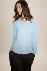 Camisa de cuello solapa y escote en pico, con manga larga y cierre frontal mediante botones. Presenta un diseño fluido con bajo asimétrico y aberturas laterales.