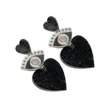Par de aros colgantes con forma de corazón y ojo, color negro con glitter plateado.