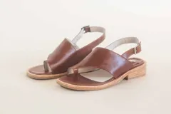 Sandalias de cuero color marrón, con tira ancha sobre los dedos, tira trasera con hebilla y suela plana.