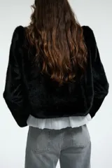 Chaqueta corta de piel sintética en color negro, con cuello redondo, hombreras marcadas y cierre frontal oculto.