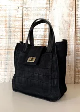 Mini bag de cuero color negro con efecto envejecido, asas de mano y detalles en cuero marrón tostado. Cuenta con un bolsillo frontal con solapa y cierre metálico giratorio, y costuras pespunteadas a la vista.