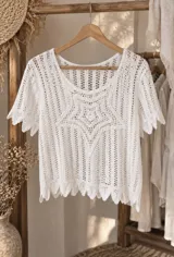 Blusa de crochet color blanco marfil con diseño calado, escote redondo y mangas cortas. Presenta terminaciones en ondas en las mangas y el ruedo.