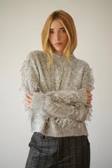 Buzo de punto color beige con cuello redondo, mangas largas con flecos decorativos y diseño de trenzas en el frente.