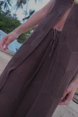 Chaleco largo de tejido de punto color marrón, con escote en V profundo y cierre frontal mediante un pequeño gancho metálico. Presenta un diseño de punto con textura geométrica y aberturas laterales.