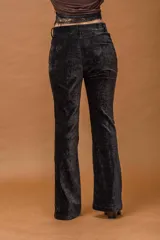 Pantalón de corte oxford confeccionado en pana negra con textura aterciopelada. Presenta un ajuste en la cadera y muslos, con una leve apertura desde la rodilla hacia el ruedo.