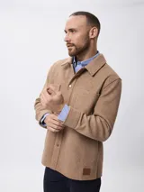 Sobrecamisa de paño color beige, con cuello clásico, cierre frontal con botones metálicos y bolsillos frontales. Presenta un diseño de corte recto y aberturas laterales en el ruedo.