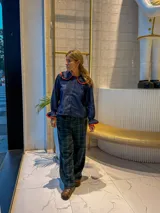 Camisa de jean azul oscuro con cuello estilo marinero y puños con volados, ambos con ribetes en color rojo. Presenta cierre frontal con botones rojos.