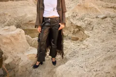 Pantalón de cuero negro con corte de jean y tiro medio, presenta apliques decorativos de rosas en la parte delantera.