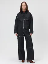 Campera de denim grueso en color negro con costuras en contraste. Presenta cuello de solapa en pana, cierre frontal con cremallera, mangas desmontables con cierre en los hombros y bolsillos de parche en el frente.