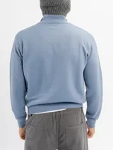 Buzo de tejido de punto color azul con textura jaspeada, cuello alto con cierre frontal parcial y puños acanalados.