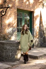 Poncho de lana merino color verde oliva, con diseño de tejido de punto, corte asimétrico y flecos en el ruedo.