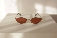 Lentes de sol con montura metálica dorada y cristales de forma geométrica (diamante/hexagonal) en tono marrón. Las patillas son doradas con puntas negras.