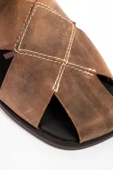 Sandalia de cuero con diseño de tiras cruzadas en el empeine y tira trasera con ajuste. Presenta un acabado rústico y suela plana de goma.