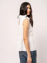 Blusa blanca sin mangas, con cuello alto con volados y detalles bordados con motivos florales.