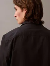 Camisa negra de manga larga con cuello abotonado y logo de Calvin Klein bordado en el pecho.