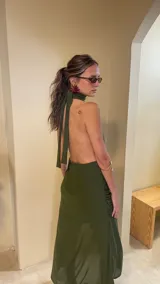 Vestido largo de microtul color verde militar, con escote profundo en V, cuello halter y detalle de choker incorporado. Falda cruzada con frunces laterales, tajo pronunciado con volados y transparencias.