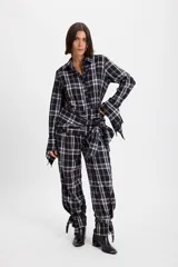 Camisa de manga larga con diseño de cuadros, confeccionada con piezas rectangulares que alternan la dirección del estampado. Presenta tajos en las mangas y en el cuerpo que permiten anudar la prenda para un ajuste personalizado.