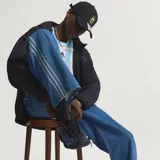 Pantalón de denim azul de corte holgado, tiro medio y diseño clásico con las tres tiras características de Adidas a lo largo de los laterales.