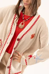 Saco tipo cardigan oversize de punto color beige, con diseño temático marino que incluye bordados de corales, peces, estrellas de mar y tortugas. Presenta detalles de galón picot en color rojo en los bordes y puños, cierre frontal con botones al tono y corte holgado.
