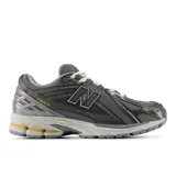 Championes New Balance modelo 1906R, color gris oscuro con detalles en gris claro, blanco y amarillo. Presentan una parte superior de malla transpirable con superposiciones sintéticas y el logo "N" en los laterales.