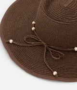 Sombrero de playa de ala mediana confeccionado en fibra de papel, con detalle de abalorios de madera en la base de la copa.