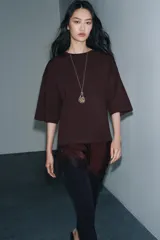 Camiseta de algodón de corte regular, color marrón oscuro o negro, con cuello redondo y manga corta. Presenta un bajo asimétrico con aplicación de encaje negro a tono.