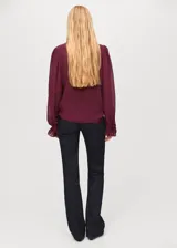Blusa de viscosa color bordó, con diseño de volantes frontales, cuello redondo con detalle de fular integrado y mangas largas con puños abotonados.