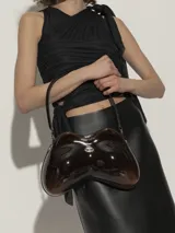 Bolso de hombro Diesel modelo Double-D, con diseño estructurado y ergonómico en forma de arco. Presenta un acabado brillante tipo charol en color negro con degradado hacia tonos más claros en los extremos, asa fija y detalle de logo metálico en el frente.