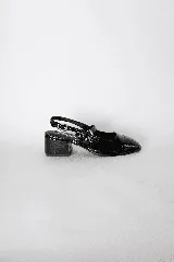 Zapato tipo sandalia con talón descubierto, confeccionado en cuero charolado negro, con taco cuadrado bajo y doble tira con hebilla metálica sobre el empeine.