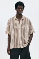 Camisa de manga corta con cuello inglés y botones frontales, confeccionada en tejido de punto pointelle con patrón de rayas verticales en tonos tierra y beige.