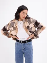 Sobrecamisa de corte holgado con estampado de cuadros en tonos beige y marrón. Presenta cuello clásico, cierre frontal con botones metálicos y dos bolsillos delanteros con solapa y botón.