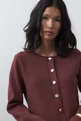 Cardigan negro de tejido de punto con cuello redondo y cierre frontal con botones a contraste. Presenta un corte entallado en la cintura con una silueta levemente evasé y mangas largas.