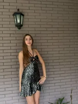 Vestido corto de lentejuelas plateadas y negras, con diseño cut-out en la cintura, escote halter con argolla central y falda con volado en el ruedo.