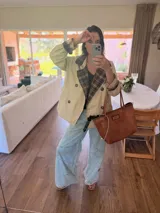 Campera tipo trench corta de gabardina color beige, con diseño de doble botonadura y solapas con forro interior a cuadros. Presenta mangas largas con puños ajustables y corte holgado.